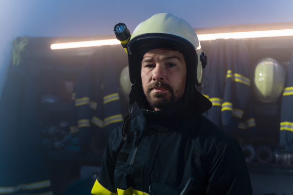 A mature firefighter preparing for action in fire station at night, looking at camera.