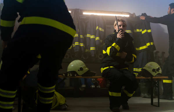 Busy firefighters men and woman getting ready for an action indoors in fire station