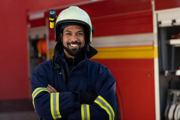 A happy young African-american firefighter man with fire truck in background.