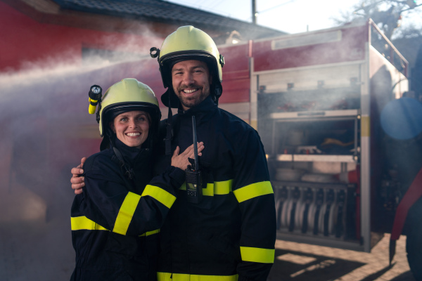 Happy firefighters man and woman after action looking at a camera with fire truck in background