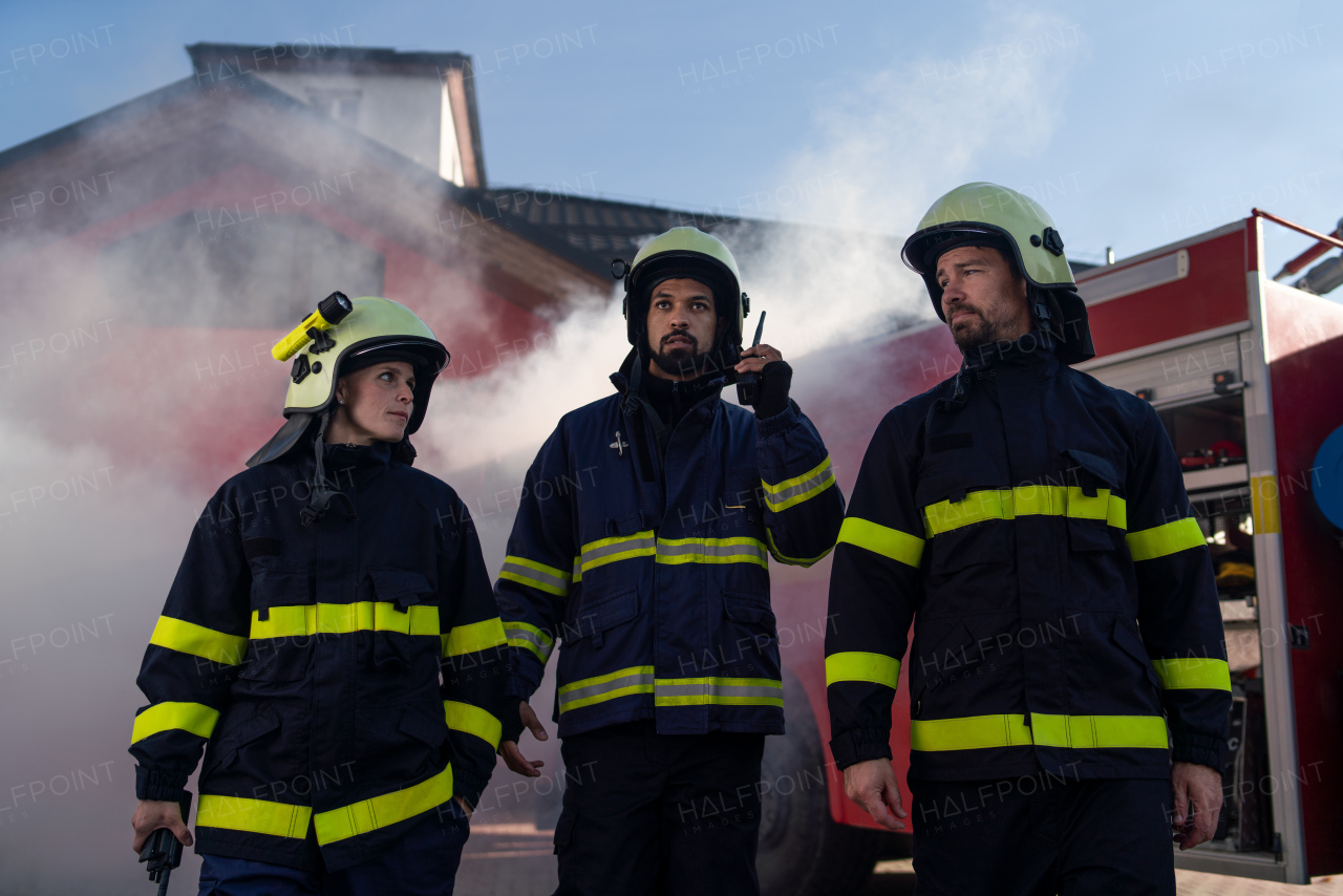 A low angle view of firefighters crew on action with fire station and truck in background