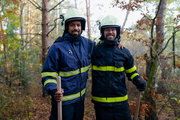 Happy firefighters men after an action, stopping fire in forest and looking at camera.