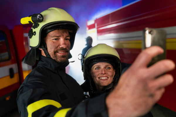 Happy firefighters man and woman after an action taking selfie with fire truck in background at night