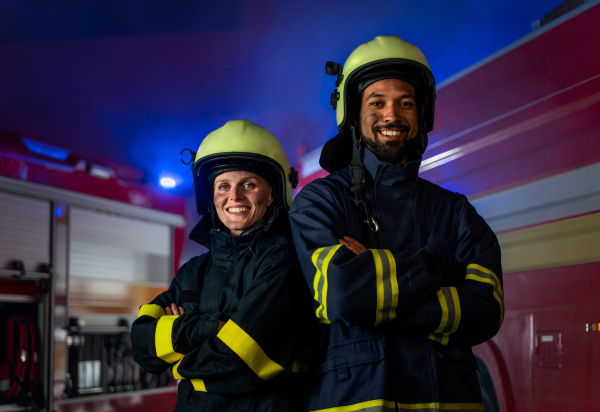 Happy firefighters man and woman after action looking at a camera with fire truck in background