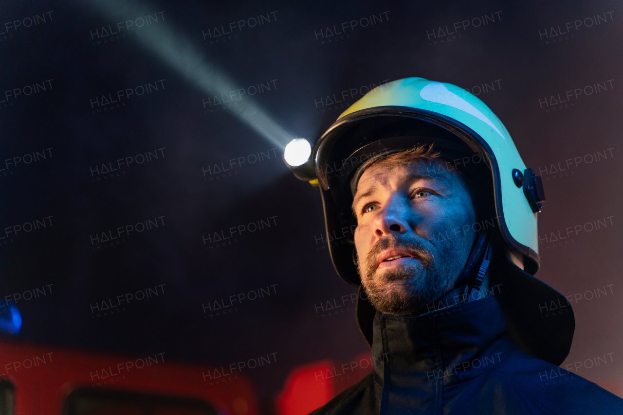 A close-up of firefighter with fire truck in background at night.