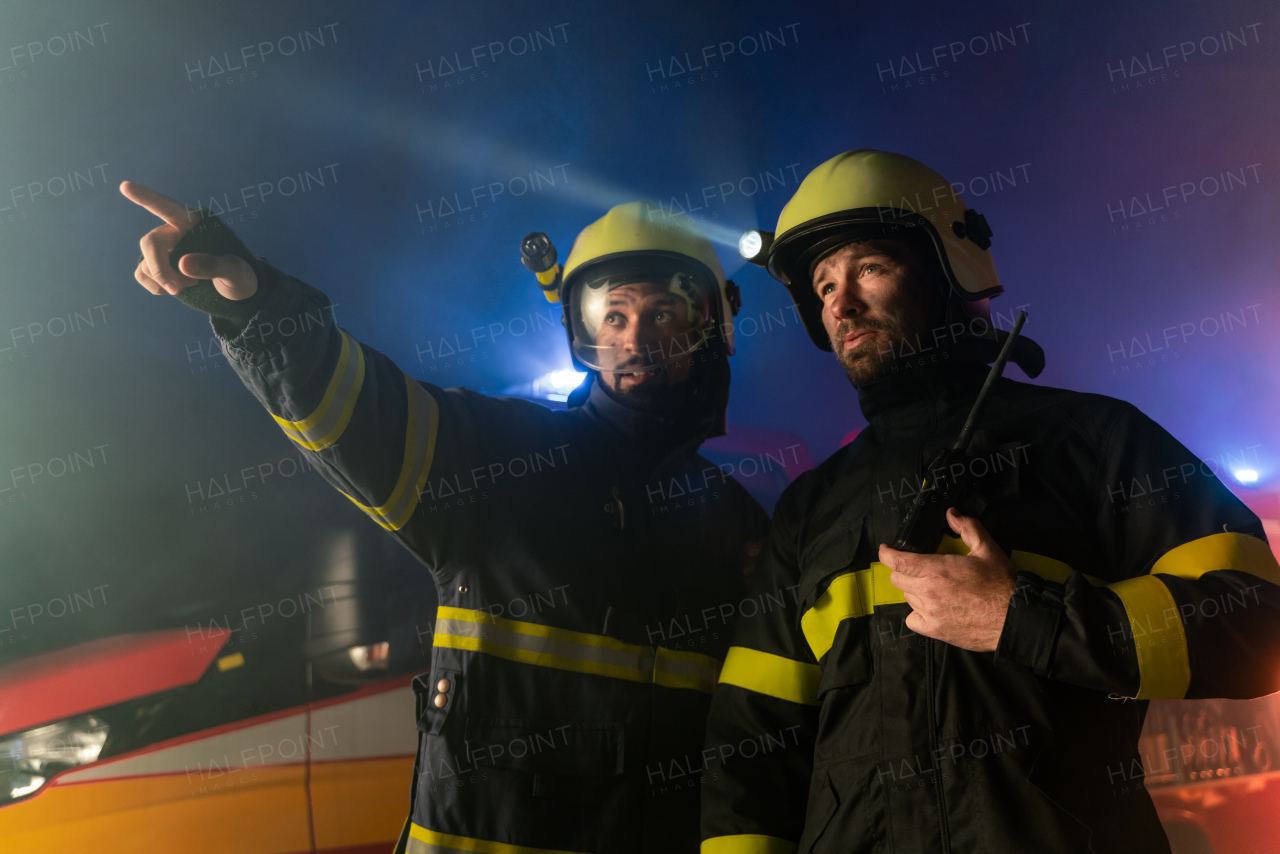 Firefighters men at action with fire truck in background at a night