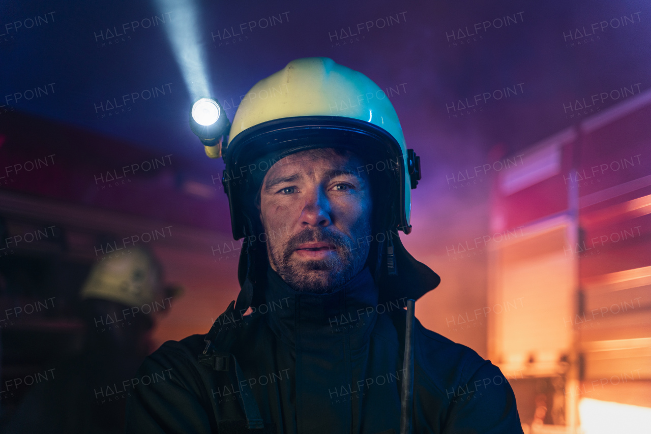 A portrait of dirty firefighter man on duty with fire truck in background at night, looking at camera.