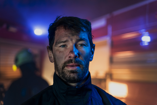 A close-up of dirty firefighter with fire truck in background at night.