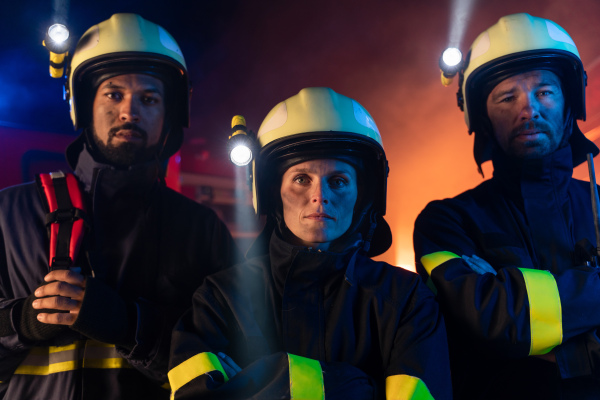 Firefighters men and woman looking at camera with a fire truck in background at night.