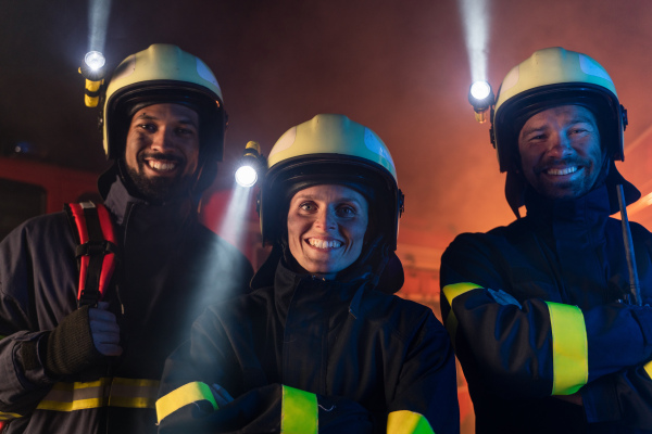 Firefighters men and woman looking at camera with a fire truck in background at night.