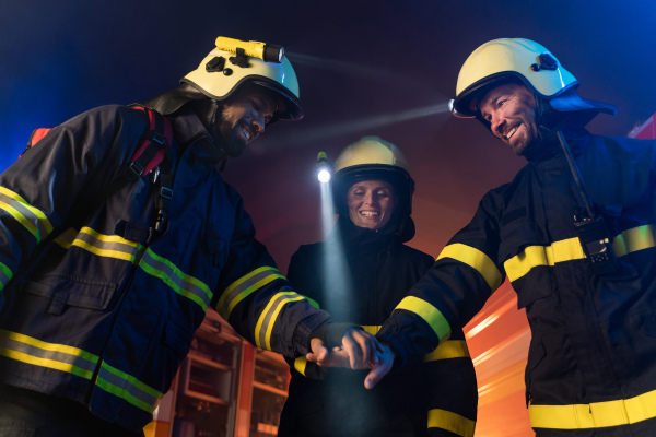 Happy firefighters men and woman after s succesful action with fire truck in background at night