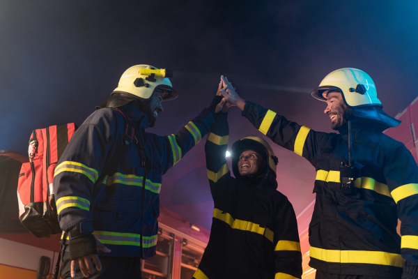 Happy firefighters men and woman after s succesful action with fire truck in background at night