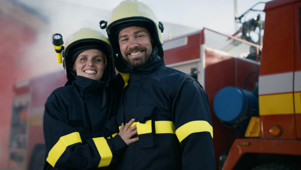 Happy firefighters man and woman after action looking at a camera with fire truck in background