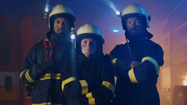 Firefighters men and woman looking at camera with a fire truck in background at night.