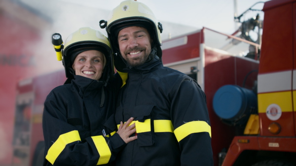 Happy firefighters man and woman after action looking at a camera with fire truck in background