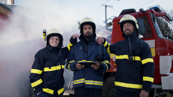 Happy firefighters men and woman after action looking at a camera with fire truck in background