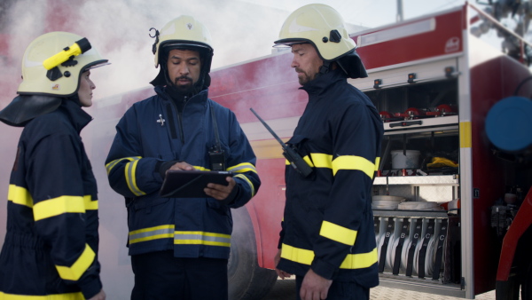 Firefighters man and woman getting instruction from chief with a fire truck in background