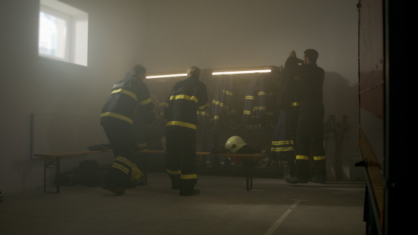 Firefighters men and womengetting ready for an action, putting on helmets and indoors in fire station at night.