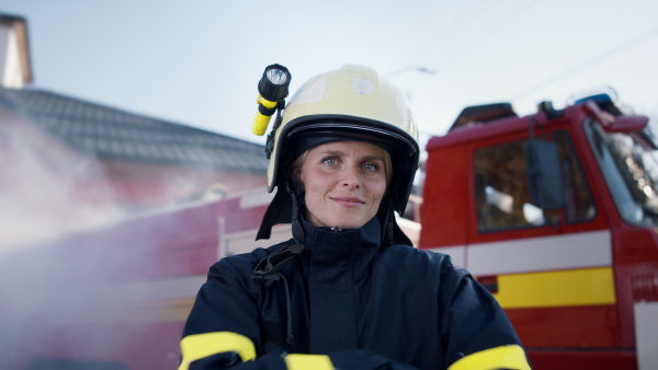 A happy mid adult firefighter woman looking at camera with fire truck and smoke in background