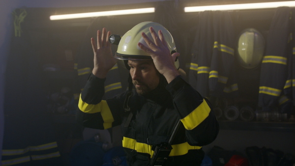 A mature caucasian firefighter putting on helmet indoors in fire station, getting ready for action at night