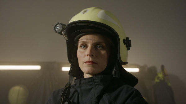 A mid adult female firefighter looking at camera indoors in fire station at night.