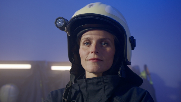 A mid adult female firefighter looking at camera indoors in fire station at night.