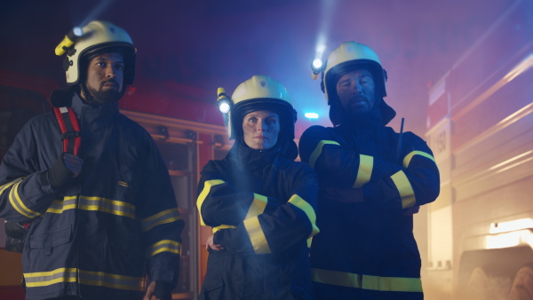 Firefighters men and woman looking at camera with a fire truck in background at night.