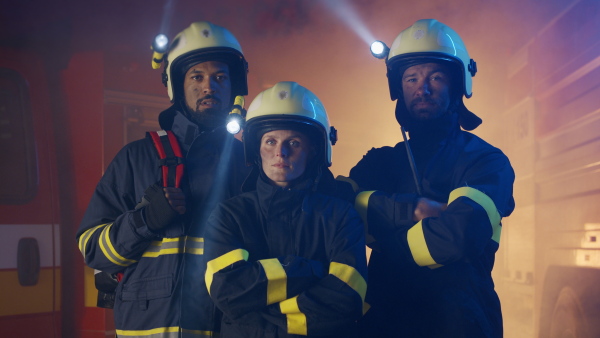 Firefighters men and woman looking at camera with a fire truck in background at night.