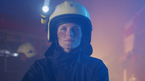 A mid adult dirty female firefighter looking at camera with fire truck at background at night.