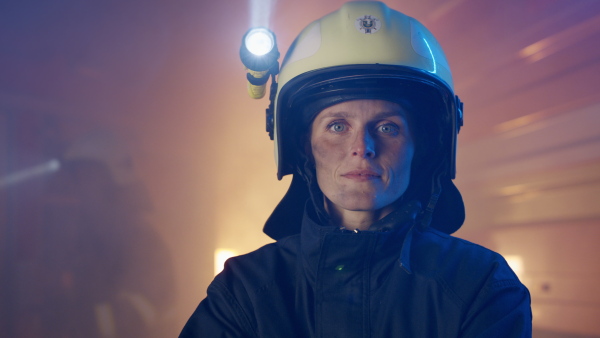 A mid adult dirty female firefighter looking at camera with fire truck at background at night.