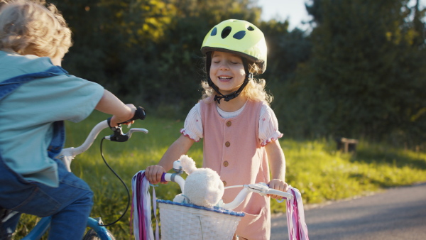 A front view of two siblings outside, riding a bike on country road.