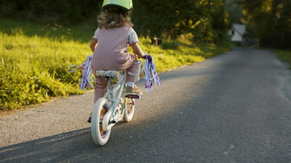 A rear view of small girl with bike helmet riding a bike.