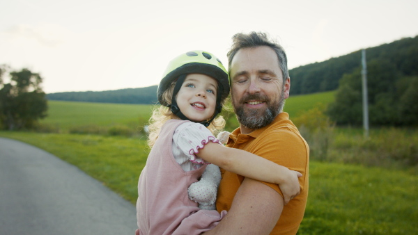 Mature father holding and hugging his daughter after bike riding training, looking at camera.