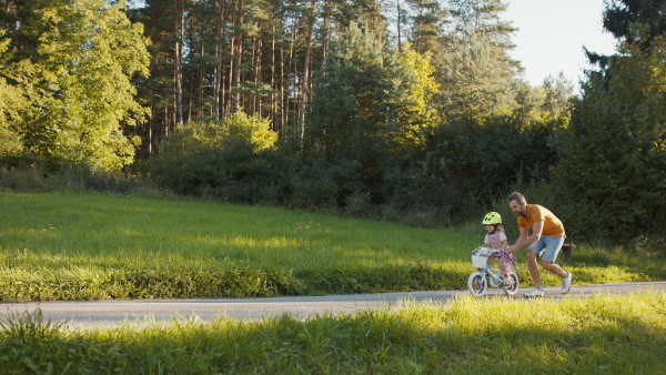 A side view of mature father teaching his daughter how to ride a bike.