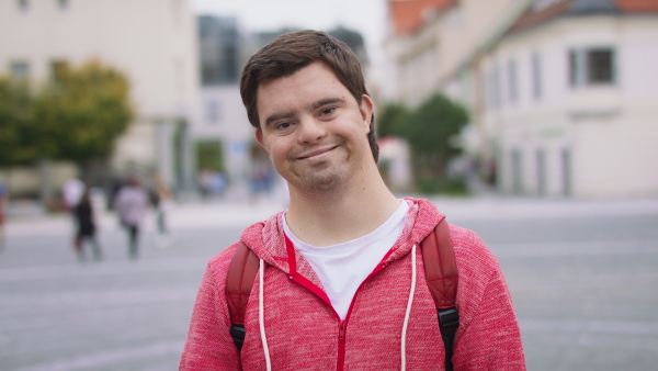 A close up of happy man with Down syndrome looking at camera and smiling outdoors in town.