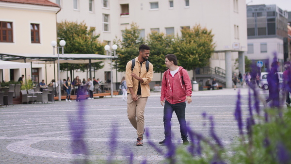 A close up of young man with Down syndrome and his mentoring friend meeting and greeting outdoors in town