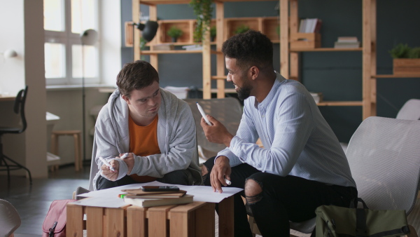 A man with Down syndrome and his tutor studying indoors at school.