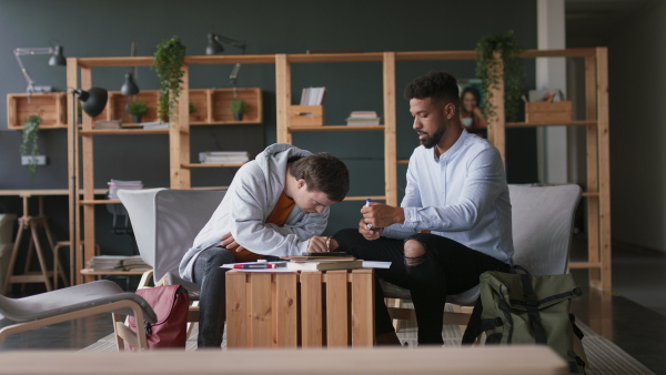 A man with Down syndrome and his tutor studying indoors at school.