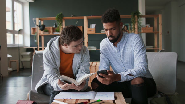 A young man with Down syndrome and his tutor studying indoors at school.