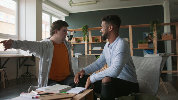 A young man with Down syndrome and his tutor hugging indoors at school.