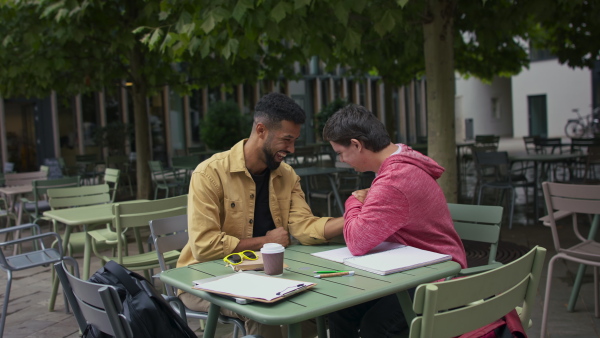 A young man with Down syndrome with his mentoring friend arm wrestling outdoors in cafe