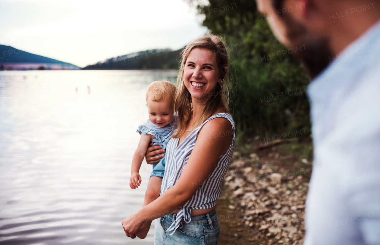 A mother with a toddler daughter outdoors by the river in summer, laughing.