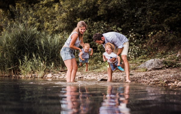 A young family with two toddler children spending time outdoors by the river in summer, having fun.