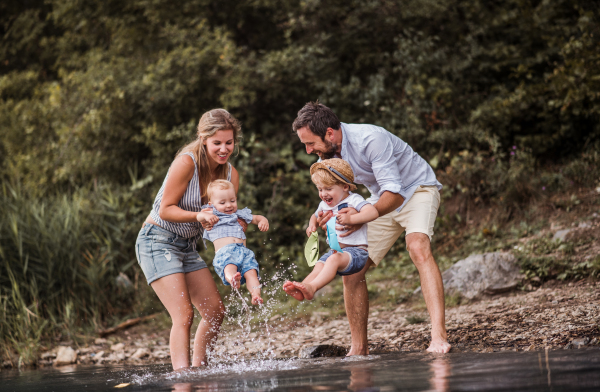 A young family with two toddler children spending time outdoors by the river in summer, having fun.