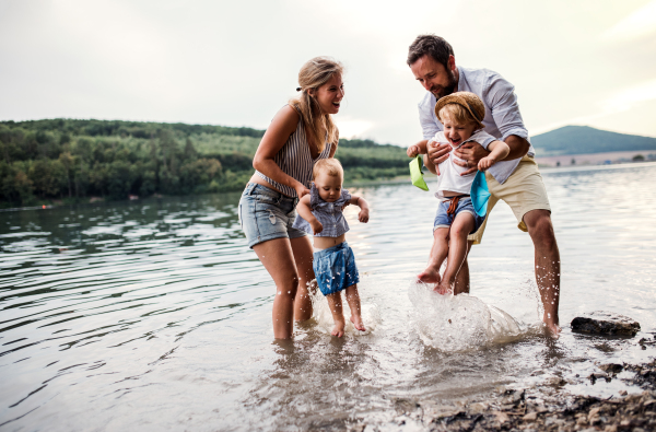 A young family with two toddler children spending time outdoors by the river in summer, having fun.