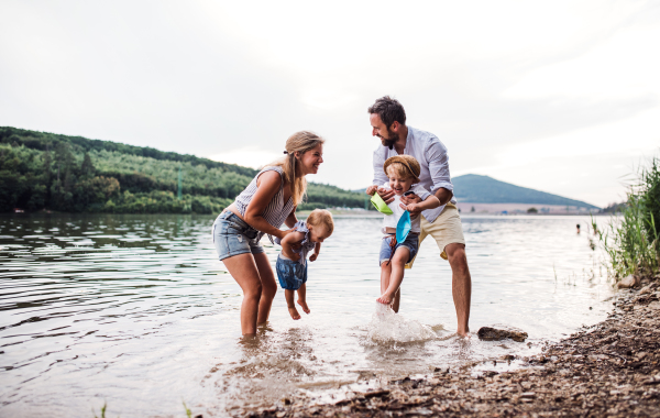 A young family with two toddler children spending time outdoors by the river in summer, having fun.