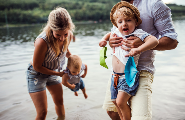 A young family with two toddler children spending time outdoors by the river in summer, having fun.