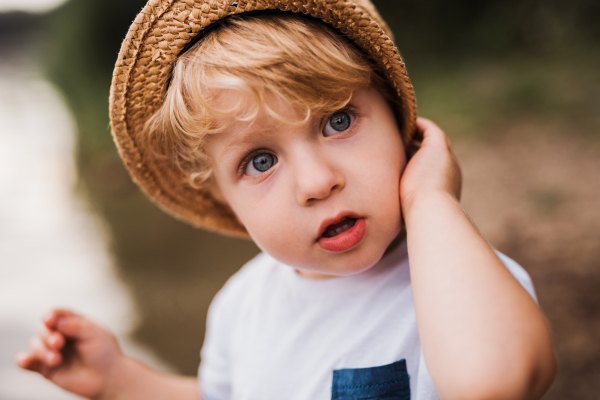 A cute small toddler boy standing outdoors by a river in summer.