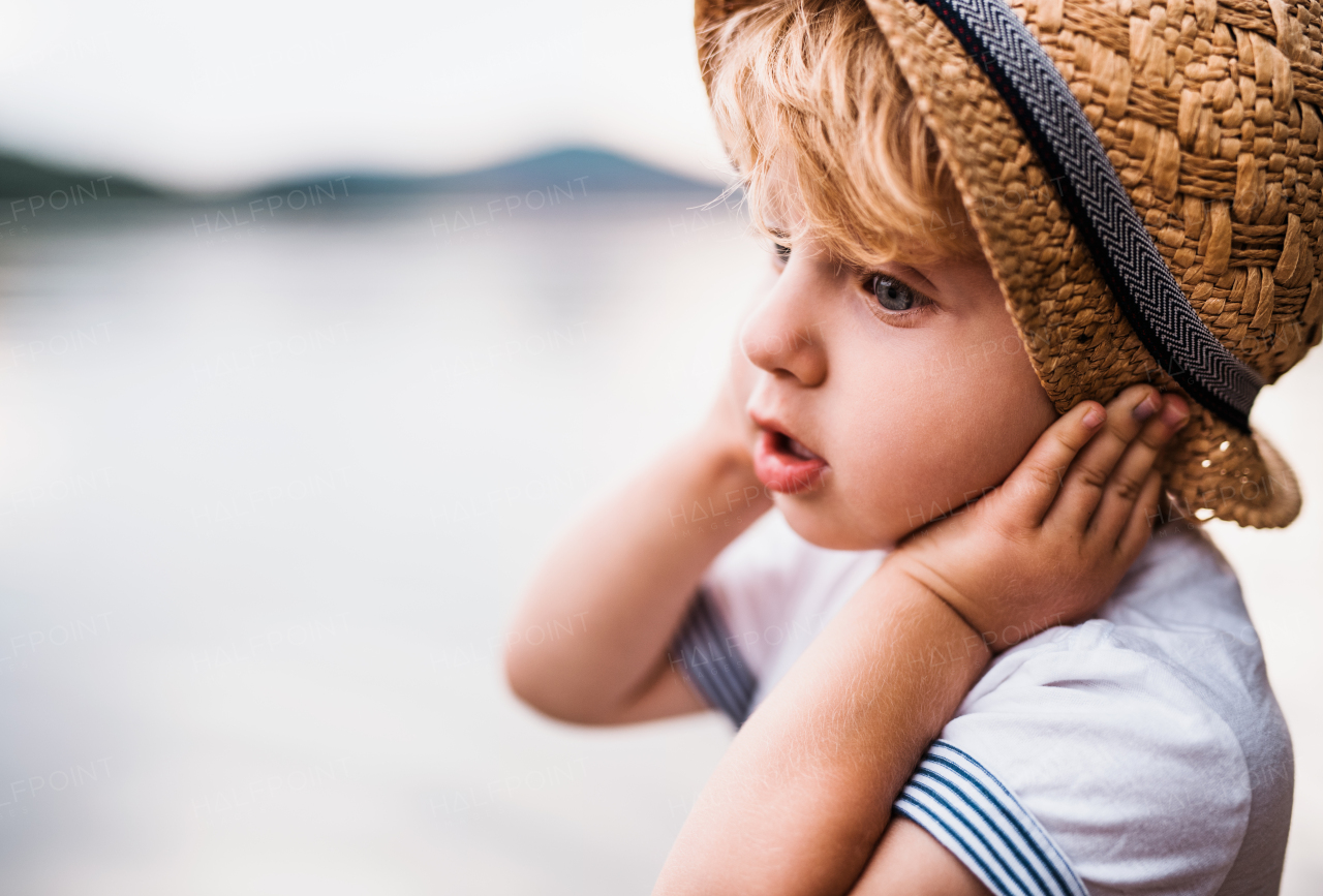 A close-up of small toddler boy standing outdoors in summer, holding a hat. Copy space.