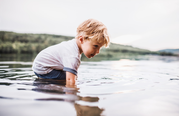 A small toddler boy playing outdoors by the river in summer. Copy space.